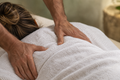 Close professional bodywork detail showing male therapist hands over a client’s towel-covered shoulders